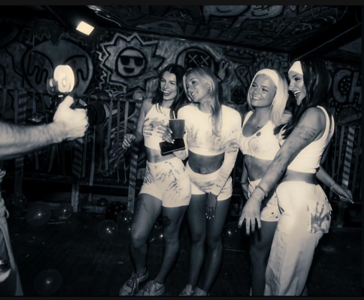 Four performers posing together while a camera operator frames the shot.